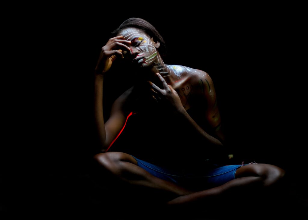 Expressionistic portrait of a woman with face paint in dark setting, showcasing emotion and solitude.